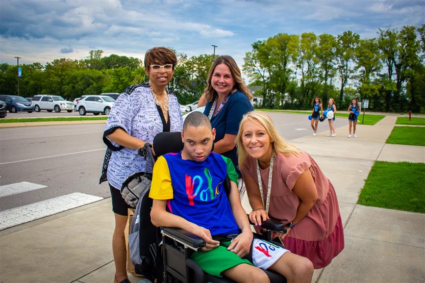 Staff members smile while standing next to a student